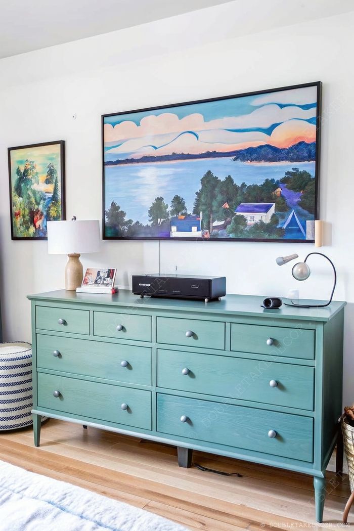 Stilvolle, mintgrüne Kommode mit Metallknöpfen unter einem bunten Meeresbild in einem gemütlichen Schlafzimmer.