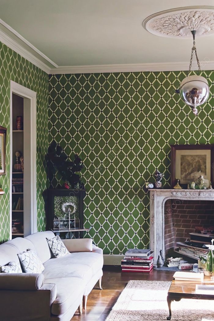 Stylish living room with diamond-patterned green walls, curved gray sofa, wooden bookshelf, and classic marble fireplace.