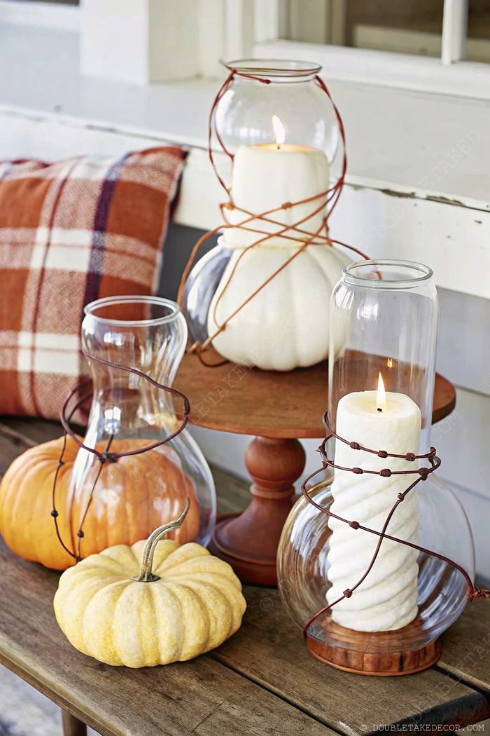 Cozy fall table display with glass containers, candle, white, orange, and pale yellow pumpkins on a rustic wooden table with plaid accent.