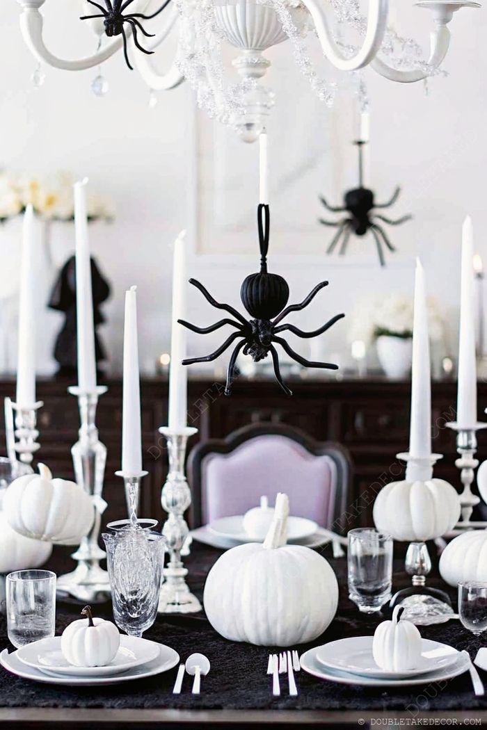 Sophisticated Halloween table with white pumpkins, crystal glassware and black spiders hanging from the chandelier above the black tablecloth.