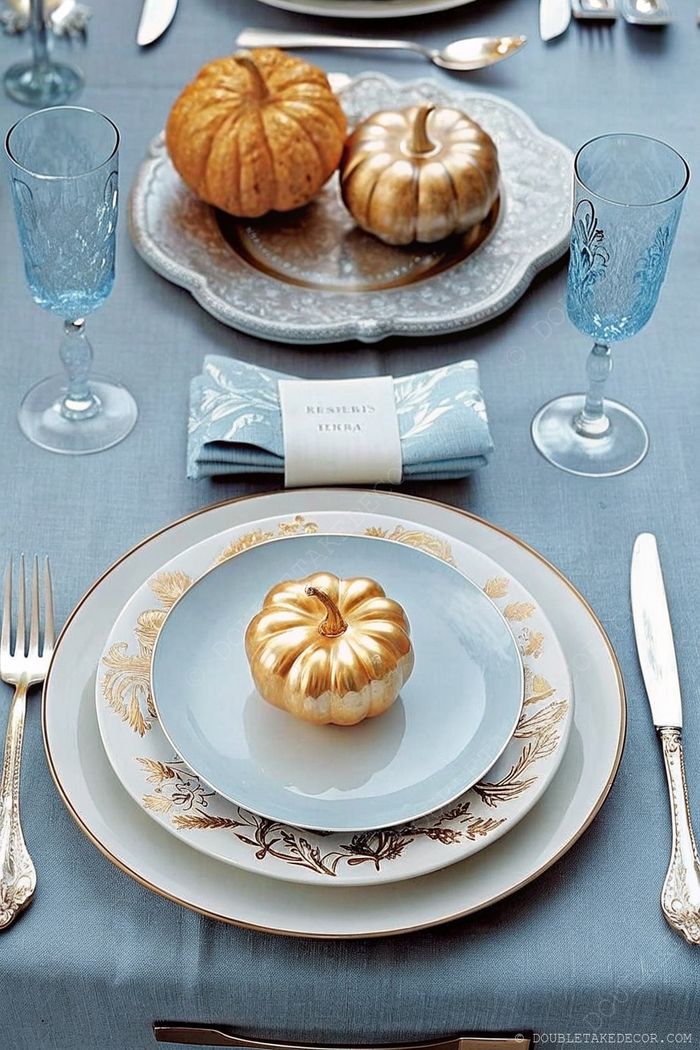 Dining table with blue tablecloth, stacked plates topped with golden pumpkin, crystal glasses, and 