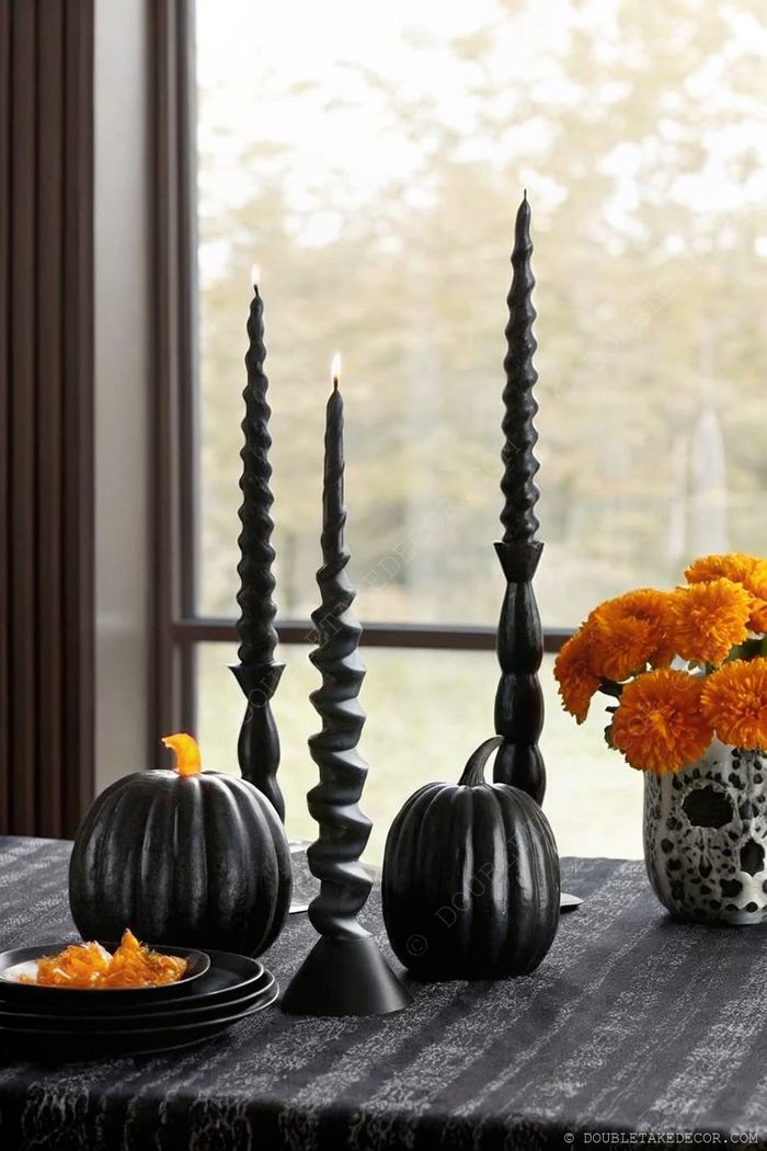Moody black tablescape with twisted candles, black pumpkins, skull vase with orange marigolds, and coordinating dinnerware for Halloween.