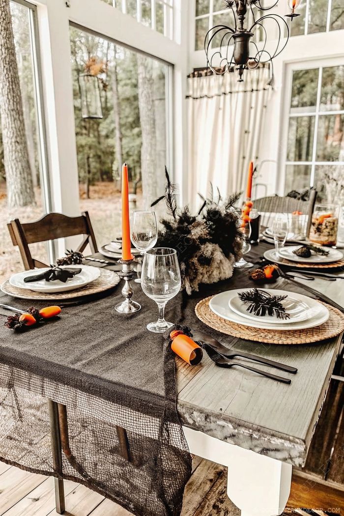 A cozy dining table with black mesh tablecloth, orange taper candles, natural placemats and black accents perfect for Halloween entertaining.