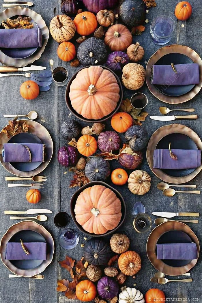 A blue tablecloth hosts an elegant autumn display with varied pumpkins, scalloped plates, blue napkins, and golden flatware for a festive harvest gathering.