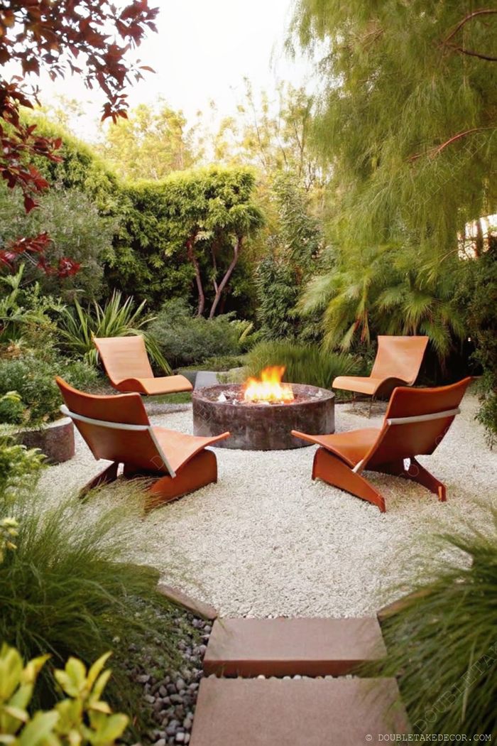 Round fire pit with white gravel surrounded by modern leather chairs amid lush greenery, creating a serene outdoor gathering space.