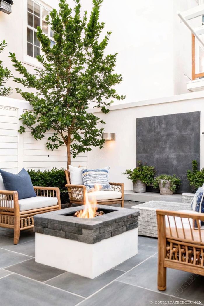Modern outdoor living space with stone fire pit, light wood seating with blue and white cushions, and elegant landscaping