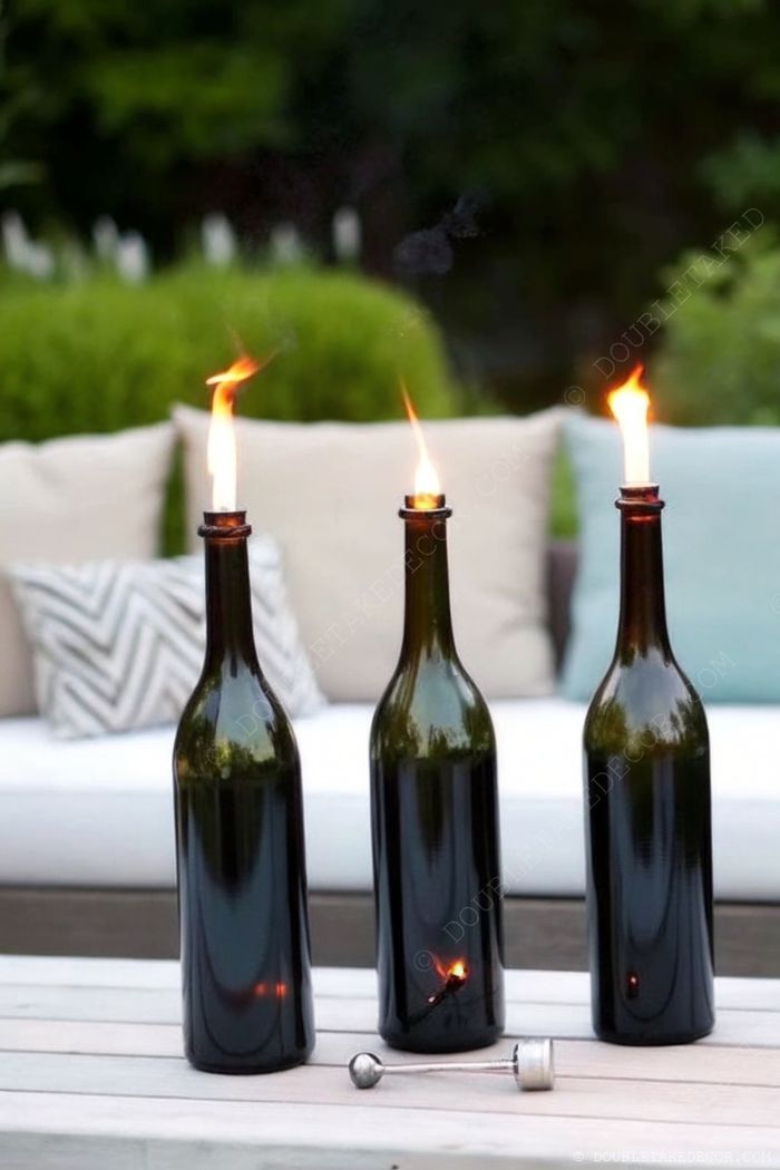 Repurposed green wine bottles transformed into elegant outdoor torches with flickering flames, arranged on a wooden table in a cozy garden setting.