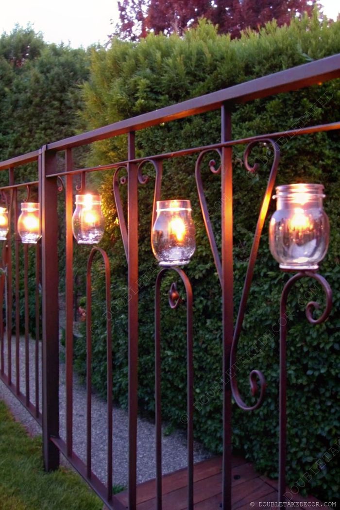 Wrought iron fence decorated with glowing glass lanterns creating a warm ambiance against lush garden greenery