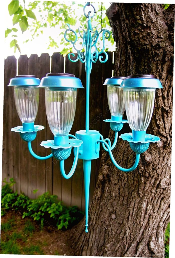 Vintage-style outdoor chandelier in vibrant turquoise with flower-shaped glass shades and decorative scrollwork against a garden backdrop