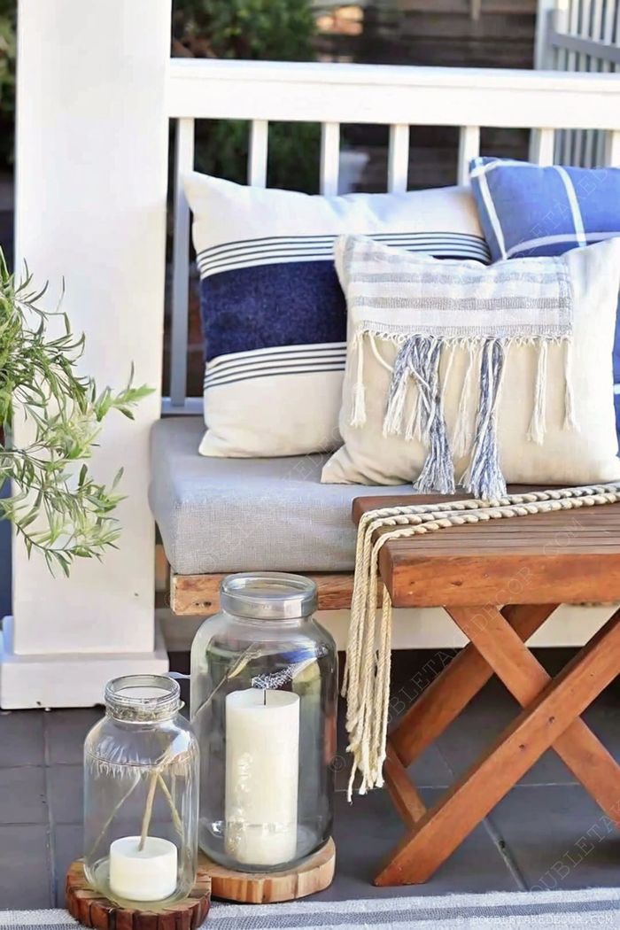 Inviting outdoor seating area with cushioned bench, decorative pillows, glass lanterns with candles, and a potted plant creating a warm ambiance.