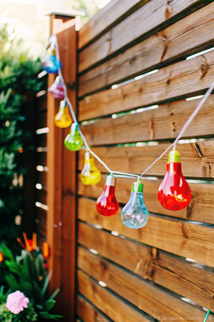 Colorful decorative lights strung across a wooden fence, with vibrant red, blue, yellow and green bulbs creating a warm, festive outdoor atmosphere.