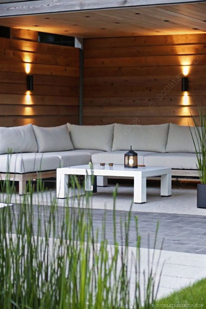 Illuminated outdoor seating area with L-shaped gray sectional, ambient lantern, and integrated wooden panel lighting