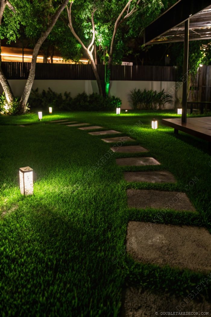 Stone pathway through a lush lawn, elegantly lit by decorative lanterns creating a warm, inviting nighttime garden atmosphere.