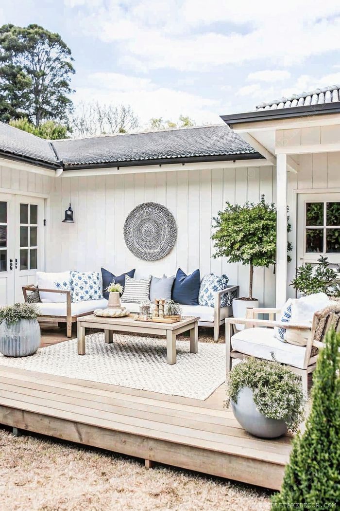 Espace de vie extérieur élégant avec canapé d’angle bleu, table basse en bois, déco murale tressée, et des plantes en pot sur un tapis texturé.