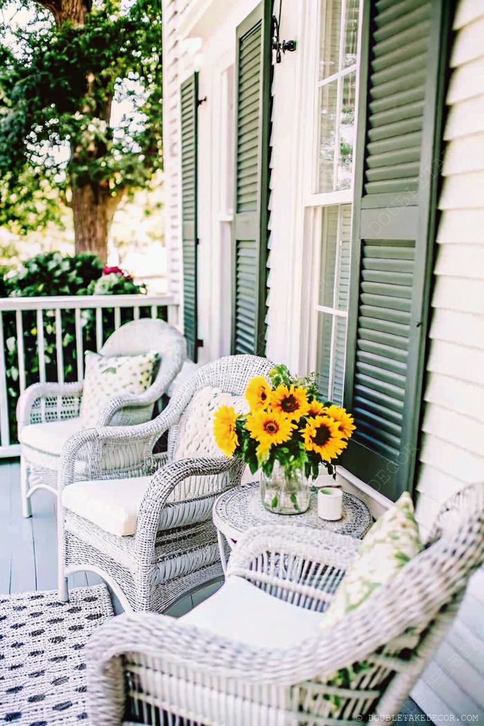 Chaises en rotin blanc avec coussins et table ronde ornée de tournesols, pour un coin paisible dehors.