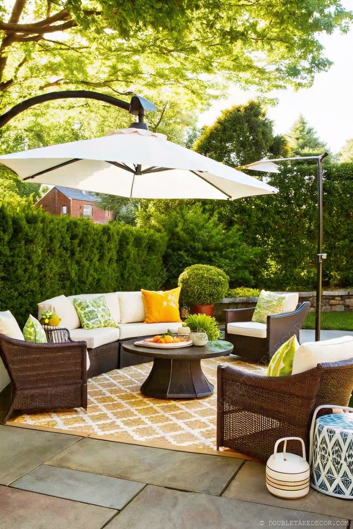 Patio élégant avec parasol blanc, canapé d’angle et fauteuils en osier sur un tapis à motifs géométriques, parfait pour recevoir.