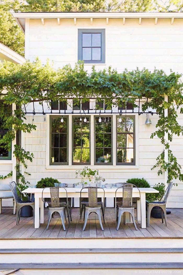 Charmant coin repas extérieur avec table rectangulaire et chaises en métal sous une pergola ornée de guirlandes lumineuses et de plantes grimpantes, parfait pour recevoir.