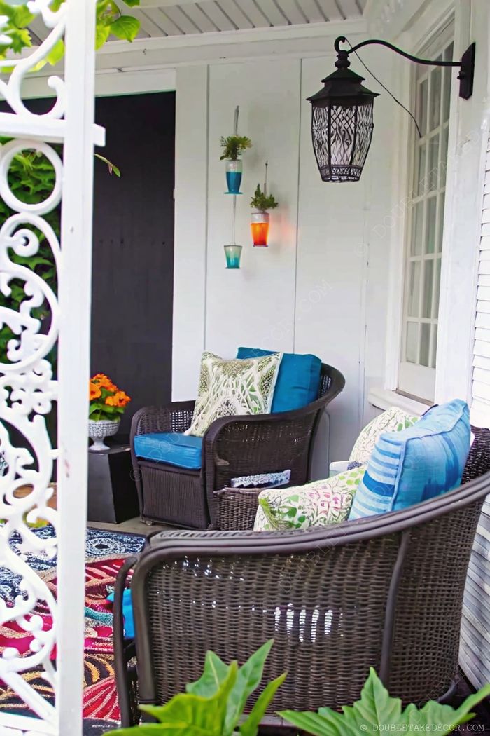 Cozy porch with wicker chairs, blue cushions, hanging glass planters, and a decorative rug creating a relaxing outdoor retreat.