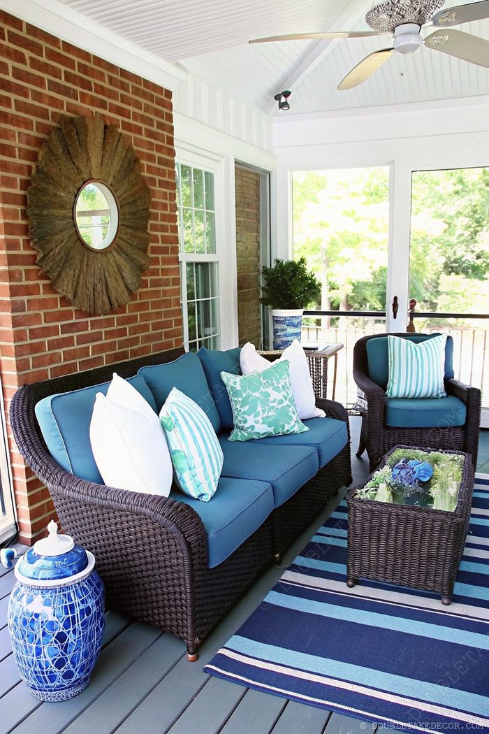 Stylish outdoor porch with dark wicker furniture, blue cushions, and decorative pillows against brick walls, creating a serene relaxation space.