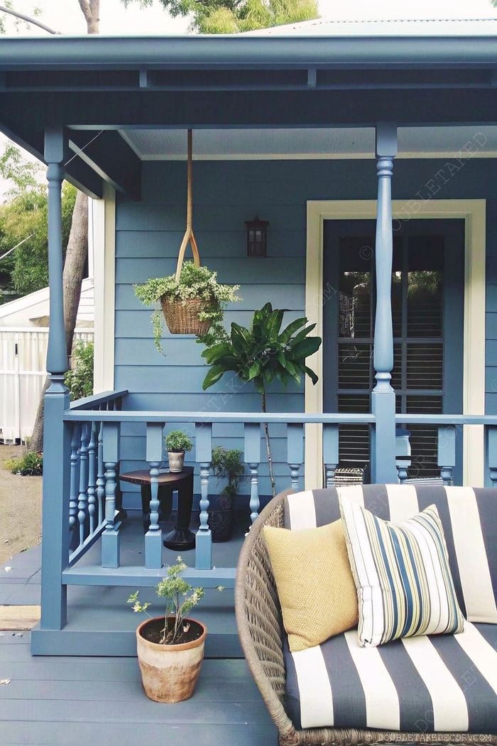 Cozy front porch with blue siding, comfortable wicker sofa with pillows, hanging plants, and decorative elements for relaxation.