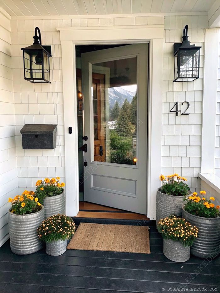Welcoming porch with gray door, black lanterns, and metal planters filled with yellow marigolds, creating an elegant, inviting entrance.