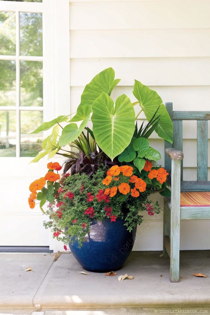 Large blue ceramic planter overflowing with colorful flowers beside a distressed teal wooden chair, creating an inviting outdoor entrance arrangement.