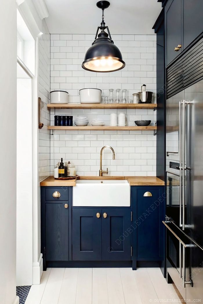 Contemporary kitchen with navy cabinetry, wooden countertop, farmhouse sink, brass faucet, and open shelving with decorative elements.