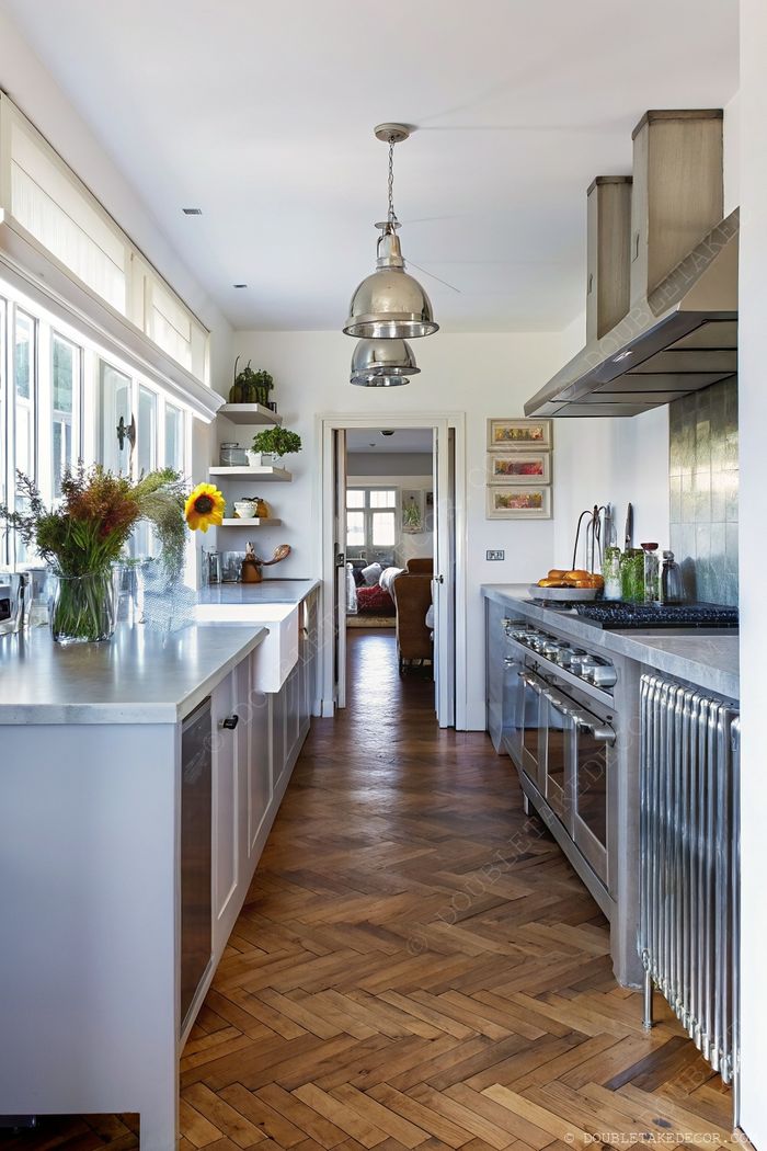 Sleek kitchen with light cabinets, concrete counters, and herringbone wood floors brightened by large windows and industrial lighting.