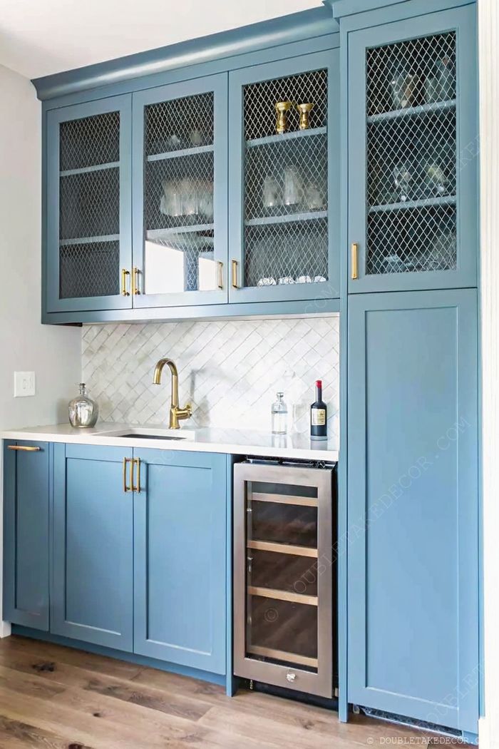 Stylish wet bar with blue cabinetry, mesh-detailed glass doors, stone countertop, gold faucet, and built-in wine cooler.
