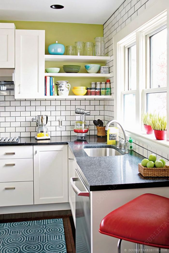 Modern white kitchen with open shelves displaying colorful dishware above subway tile backsplash and black countertops.