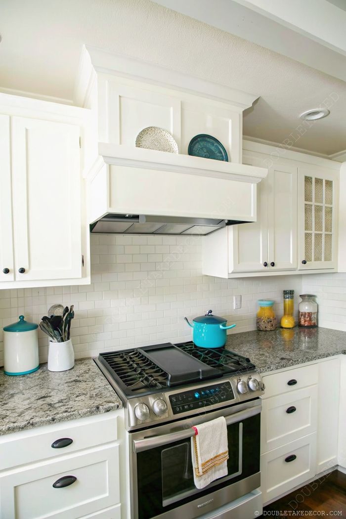Modern white kitchen with decorative plates, gray granite countertops, and colorful accents creating an inviting cooking space.