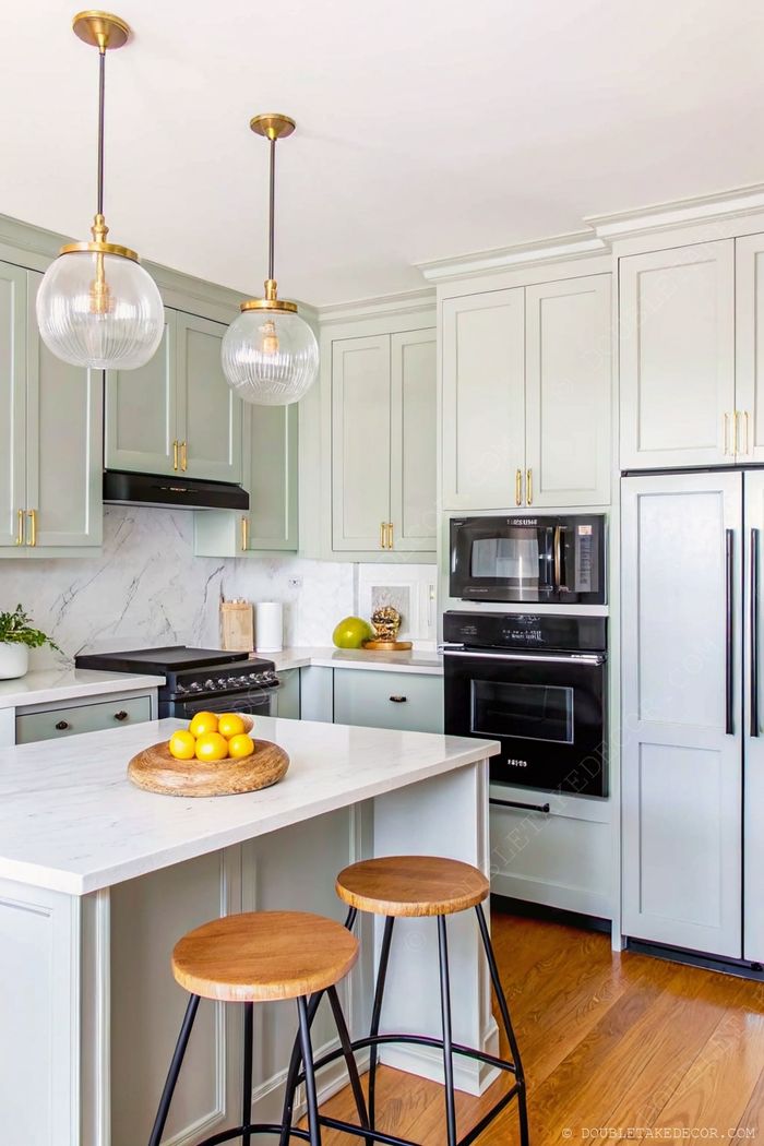 Modern kitchen with soft green cabinets, black appliances, marble countertops, and wooden accents for small space elegance.