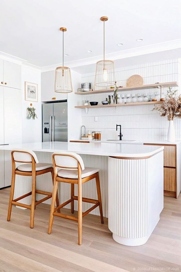 Modern white kitchen featuring a fluted island with curved edges, gold hardware, and stylish pendant lights above, creating a bright, sophisticated space.