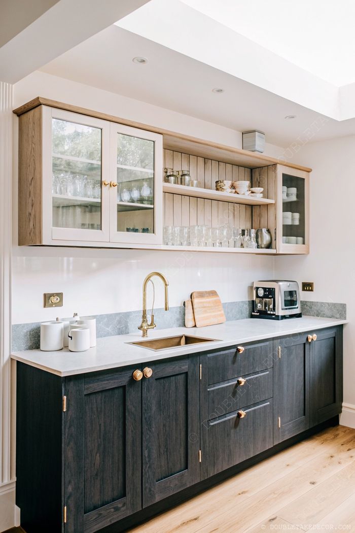 Modern kitchen with dark wood cabinets, gold hardware, open shelving, and glass-front displays illuminated by natural light.