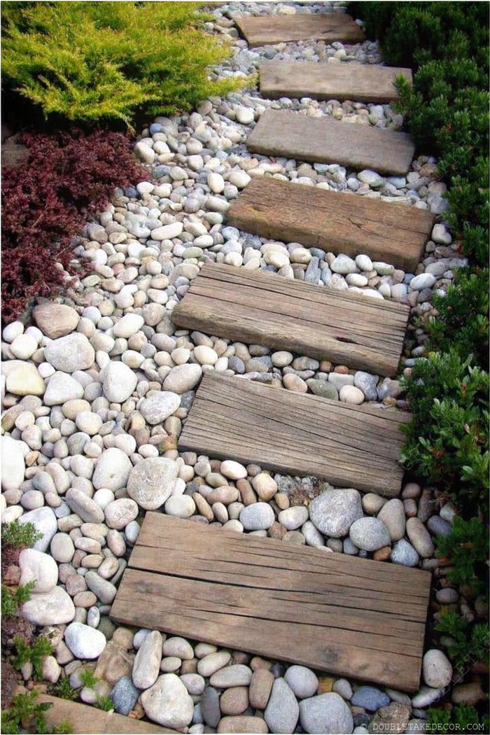 Inviting wooden rectangular stepping stones creating a straight path through pebbles and lush greenery, offering textural contrast and serene organization.