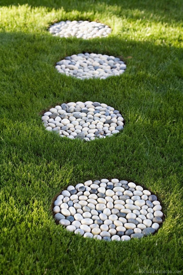 Elegant circular stepping stone pathways made of smooth white, gray, and black pebbles arranged in perfect circles across a lush green lawn.