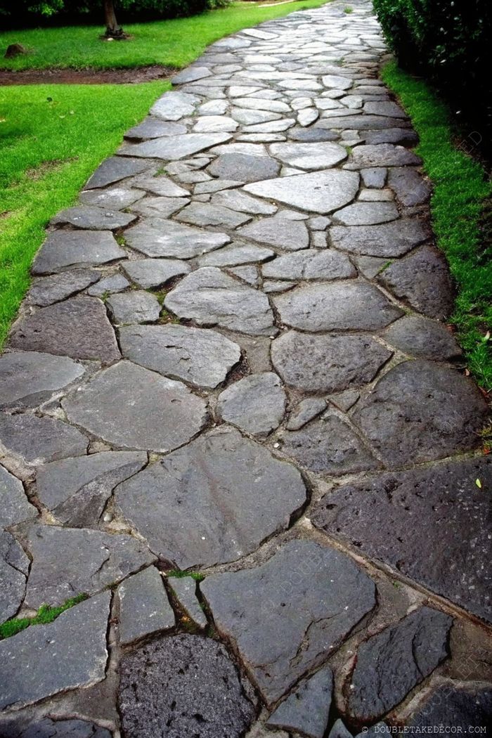 Irregular dark stones create a textured pathway meandering through lush green grass, offering a charming garden walkway.