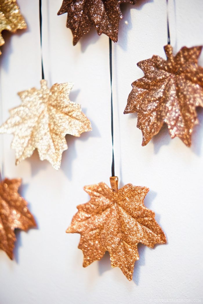 Gold, copper, and bronze glittering leaves hanging from black strings against a white wall for elegant fall decor