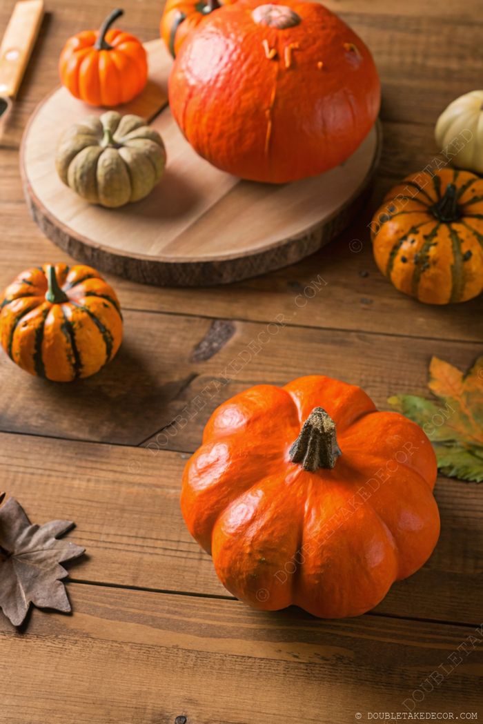 Cozy fall scene with vibrant pumpkins arranged on a wooden table, complemented by scattered autumn leaves for seasonal decor.