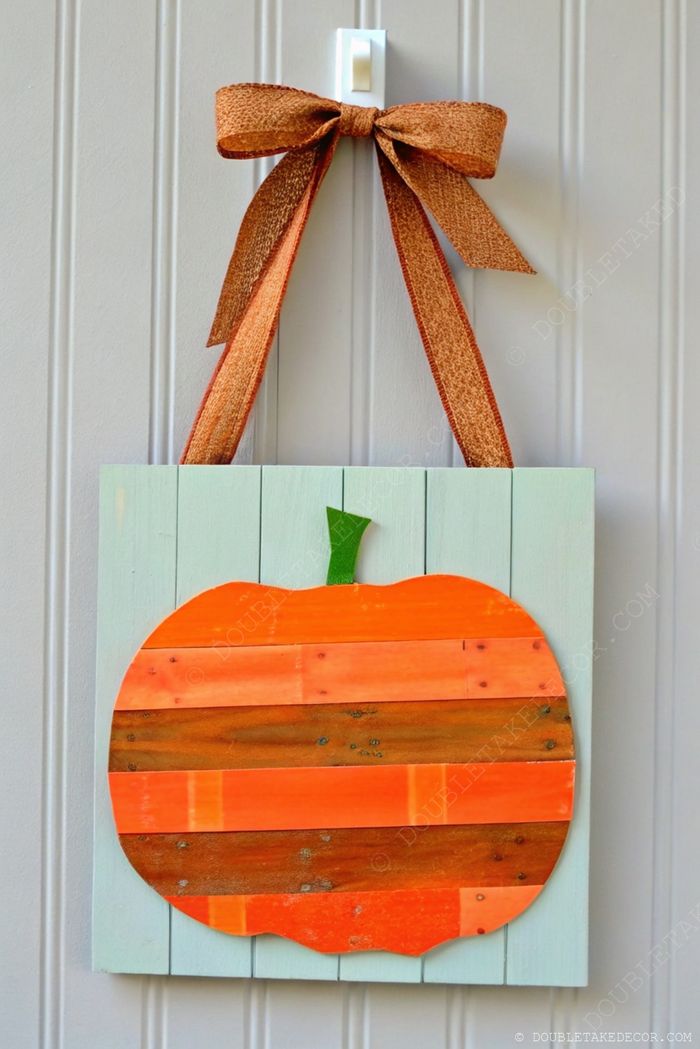 Handmade wooden plank pumpkin wall hanging with orange and brown tones, green stem, and orange bow against pale blue background