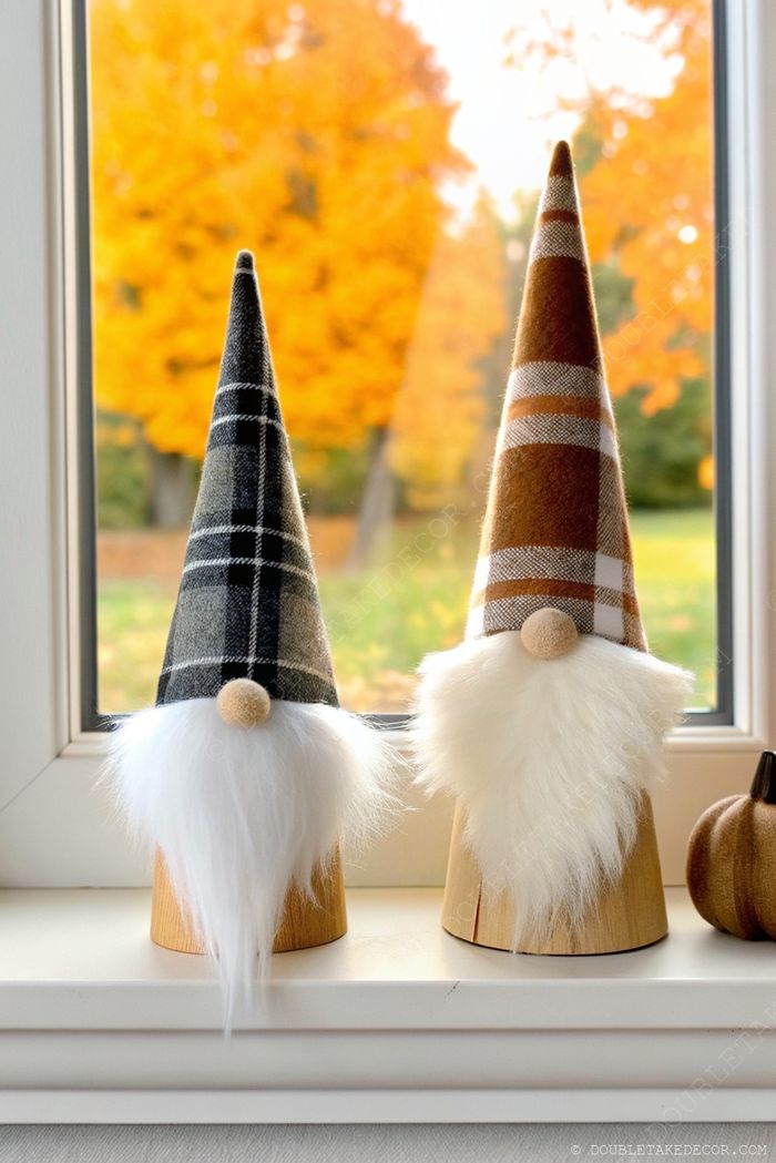 Decorative gnomes with checkered patterns and white beards sit on a wooden windowsill against colorful fall foliage.