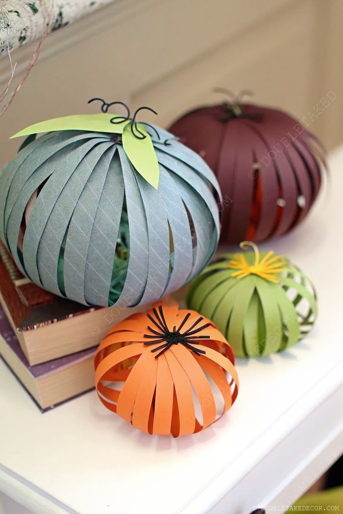 Decorative paper pumpkins in blue, purple, orange, and green with curled wire stems arranged on stacked books for autumn decor