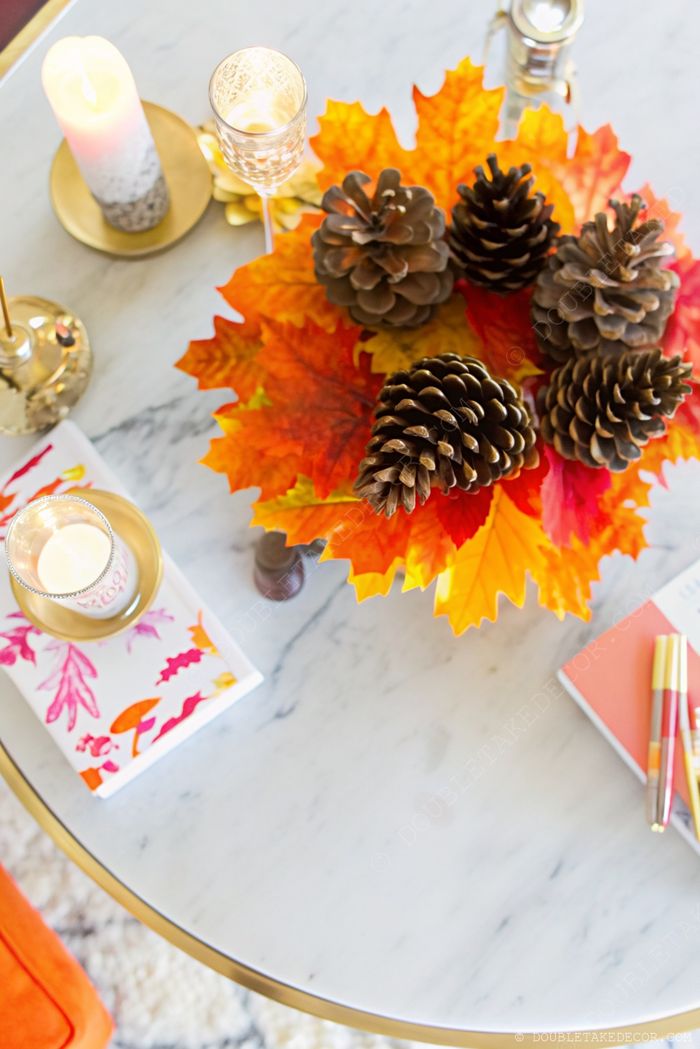 Marble coffee table with vibrant fall decor featuring faux leaves, pinecones, gold candelabrum, and decorative notebooks—perfect for autumn entertaining.
