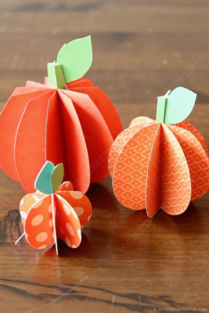 Handcrafted paper pumpkins in red, orange, and polka dot patterns with green leaves displayed on wooden table for fall decor