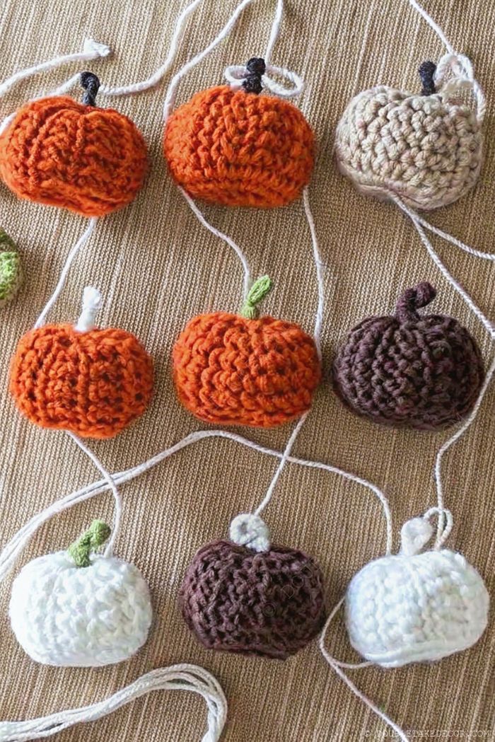 Collection of handmade crocheted pumpkins in orange, white, and brown with stems, connected by yarn for fall decor