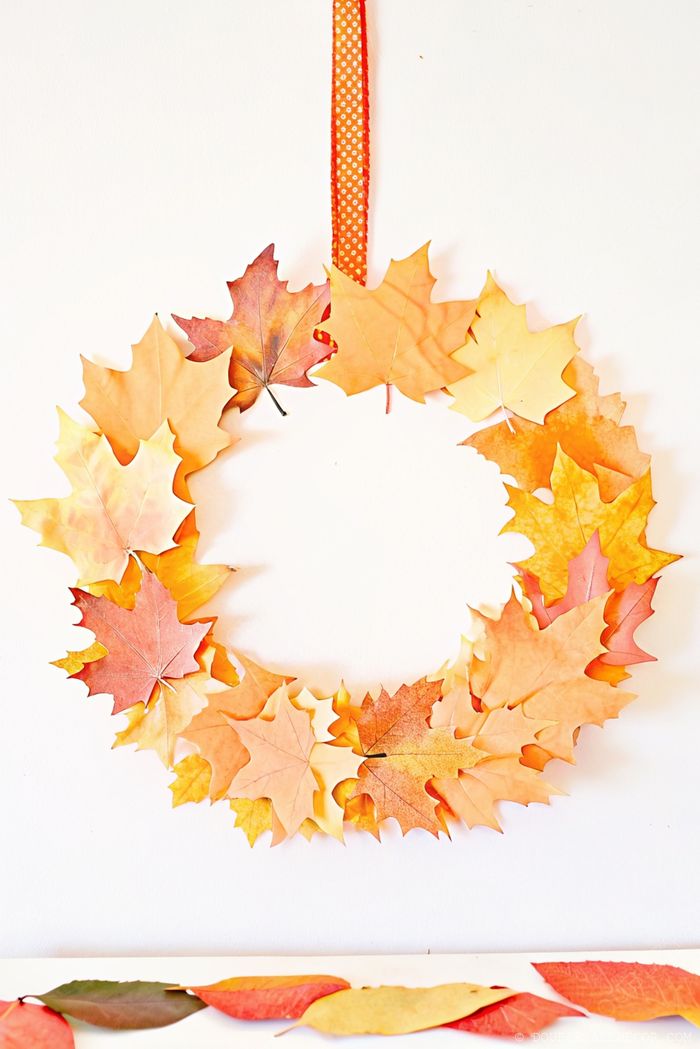 Decorative autumn wreath made of vibrant orange, yellow and red leaves with a dotted orange ribbon, perfect for fall home decor.