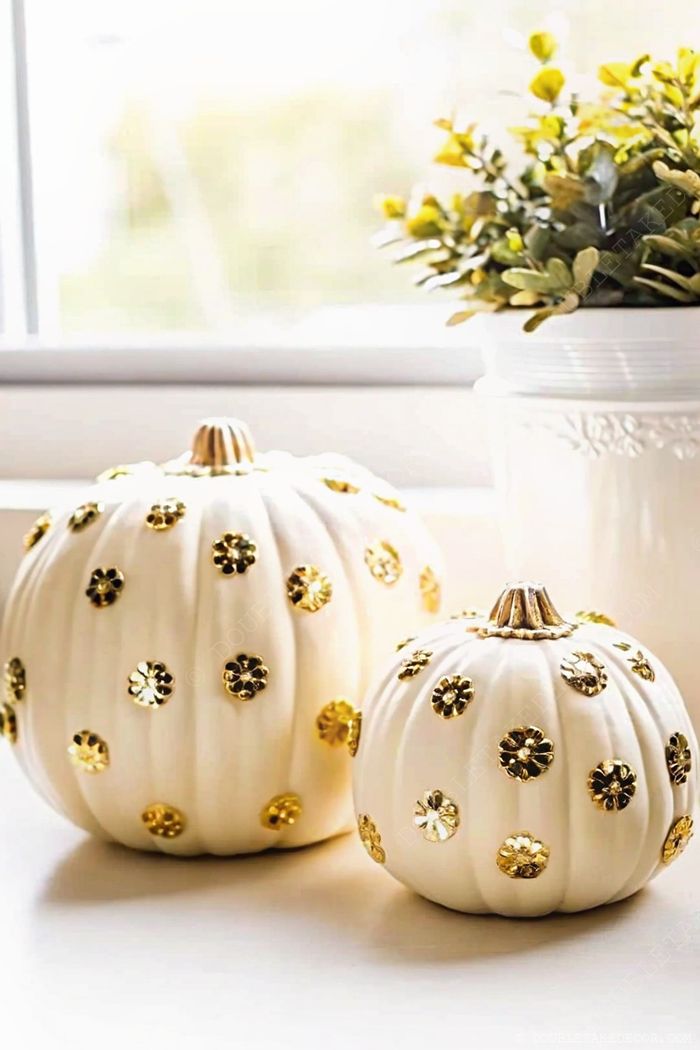Two decorative white pumpkins with golden floral embellishments arranged as an elegant fall centerpiece with a small green plant