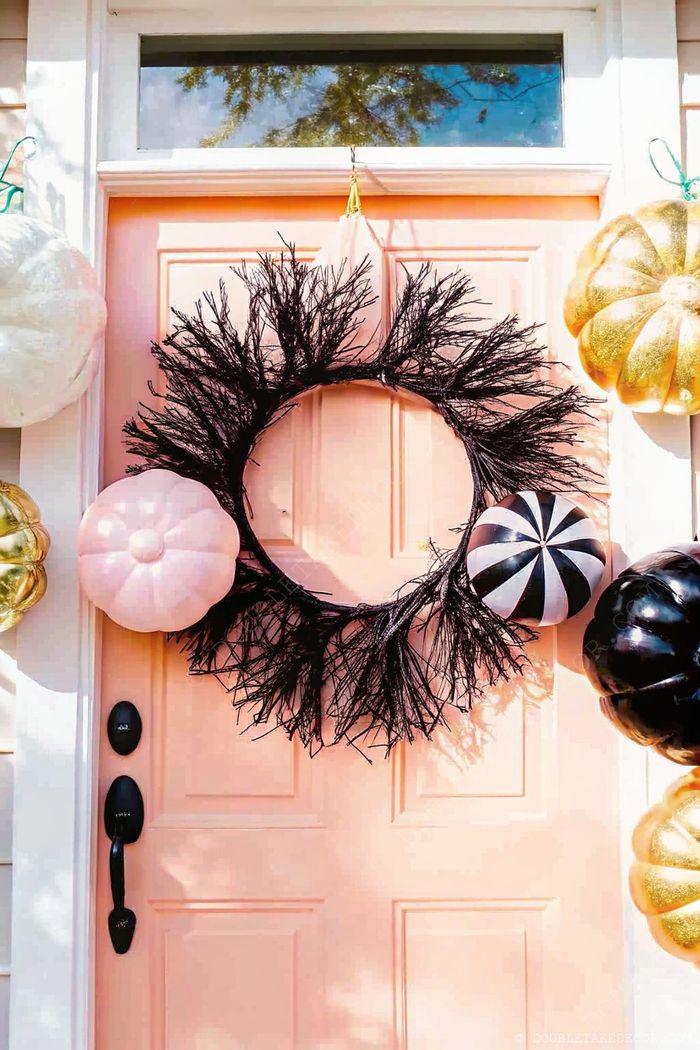Peach door adorned with black twig wreath featuring decorative pumpkins in pink, striped, and black, with additional gold glittery accents.