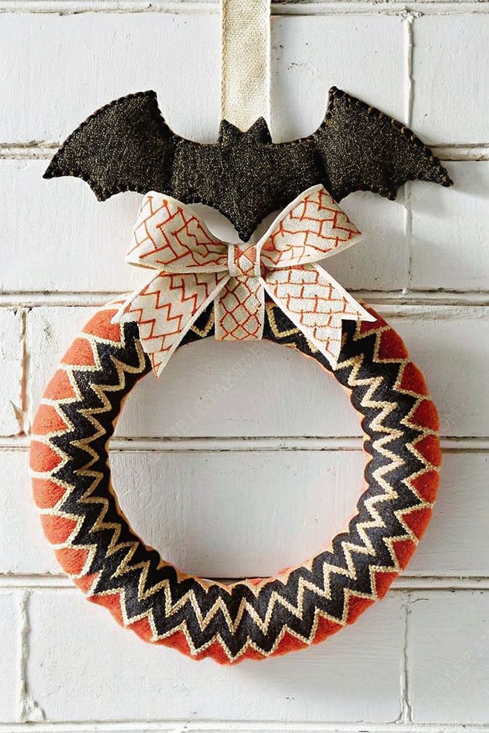 Halloween wreath with orange, black, and gold zigzag patterns, featuring a playful black bat accent and geometric ribbon bow