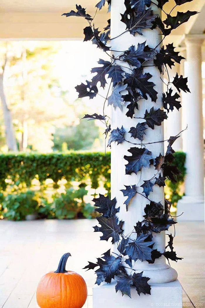 White column adorned with black leaf garland and a vibrant orange pumpkin at its base, creating a sophisticated Halloween outdoor display.